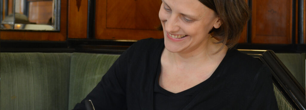 Foto von Doris Ossberger, lachend mit Blick auf Stift in ihrer Hand